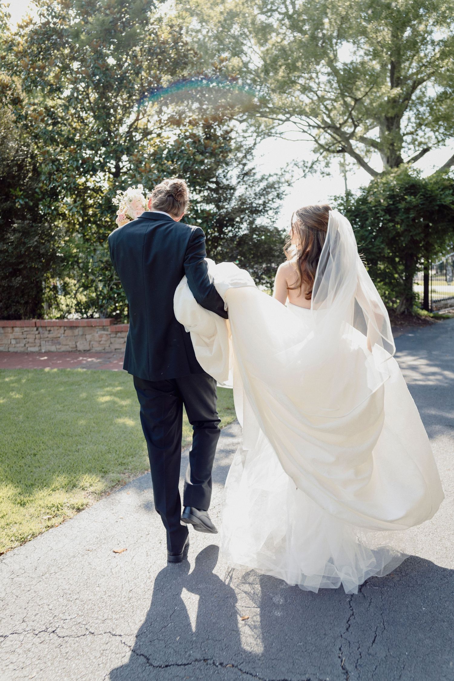 Wedding couple walking along path with bride's dress flowing in the breeze.