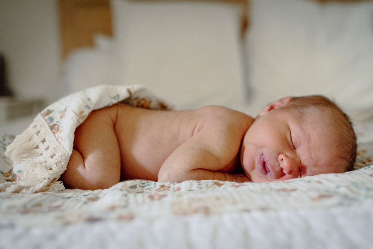 A sleeping newborn baby wrapped in soft white lace blankets.