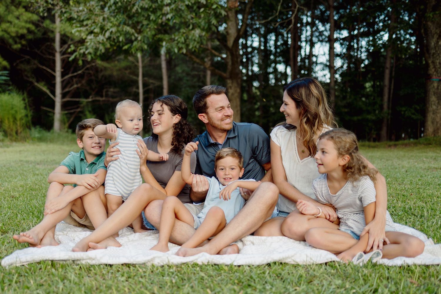 Large family cuddles on a blanket outside in golden light, natural and candid photography