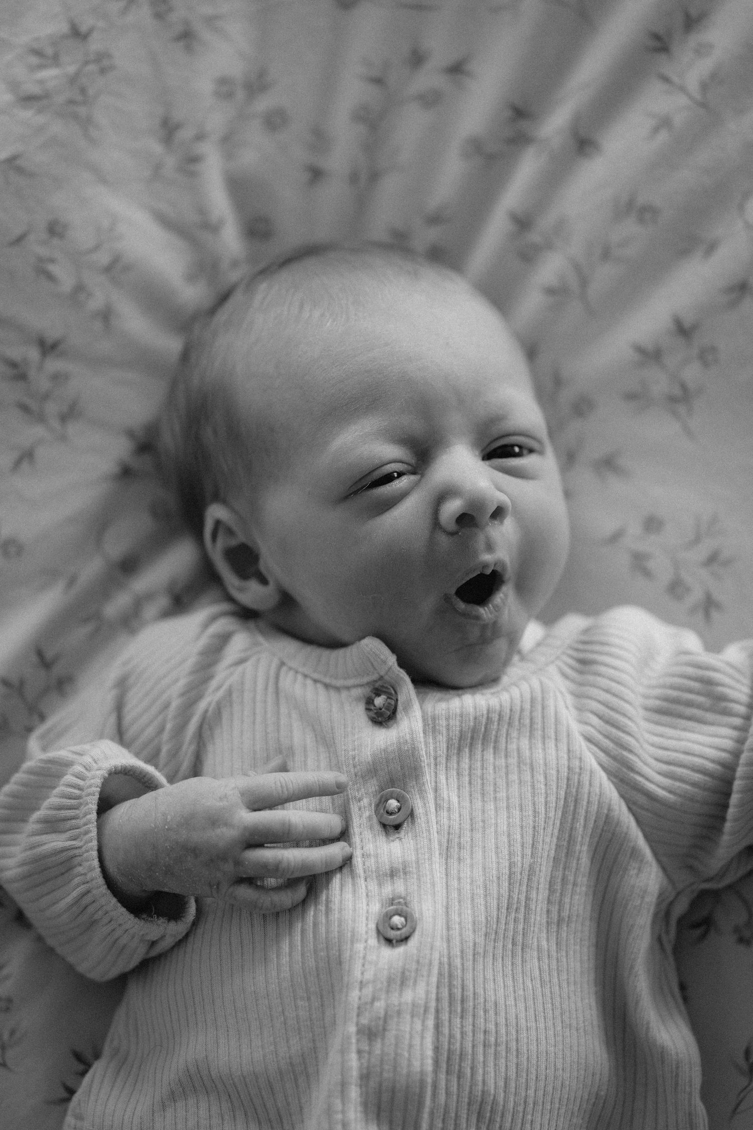 A sequence of black and white photos showing a baby yawning while wearing a white ribbed sweater.