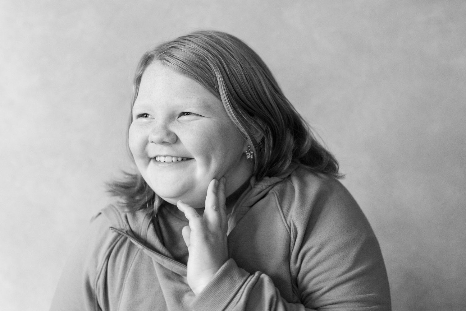 A black and white portrait of someone smiling warmly while touching their chin against a simple background.