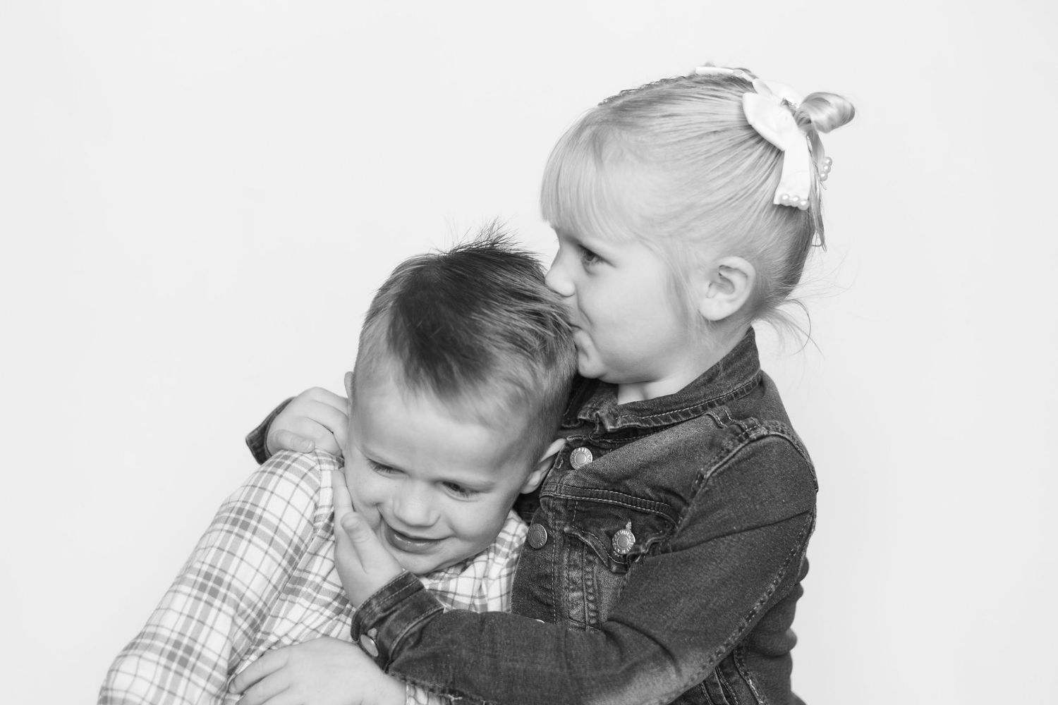 Black and white photo of two young siblings hugging, with a little girl kissing her smiling brother on the cheek.