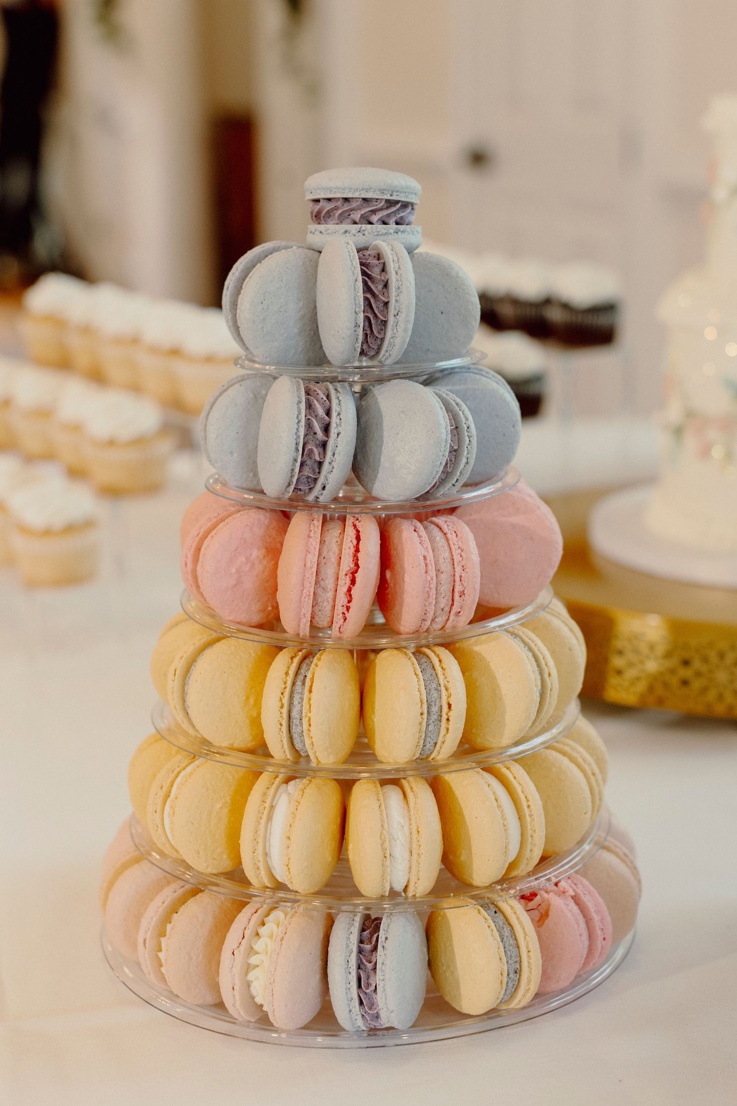 Tiered display of pastel colored macarons in pink, yellow, and blue shades for wedding dessert.