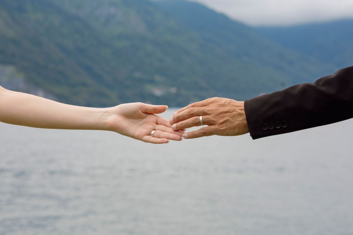 Hands exchanging rings against a misty mountain backdrop during an outdoor wedding ceremony.