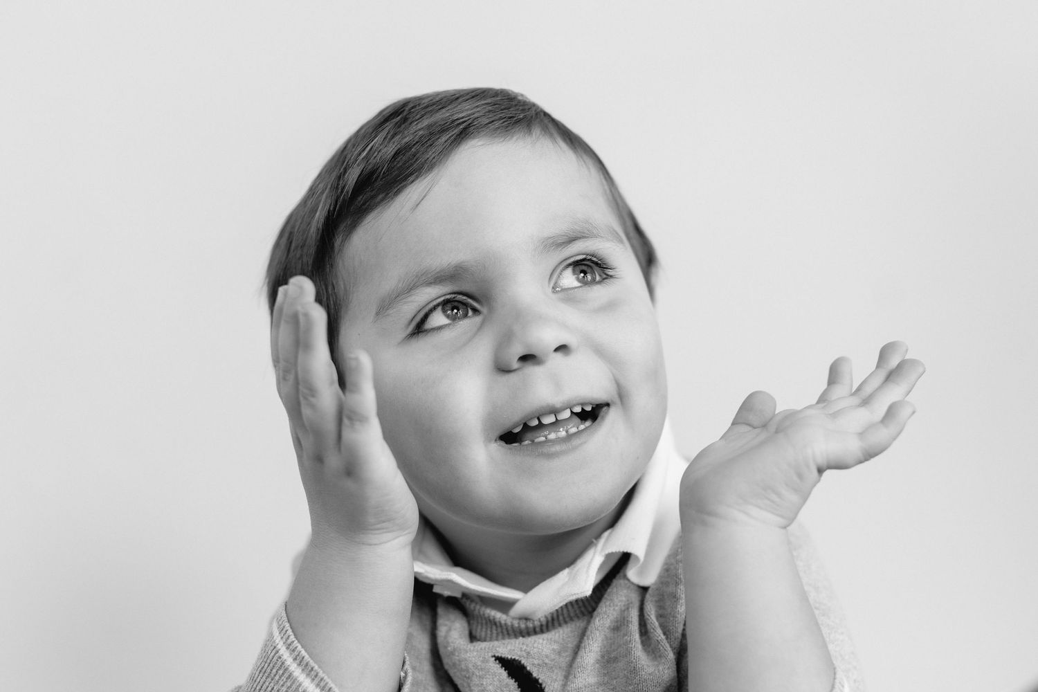 Black and white photo of a young child making an expressive face with hands raised near their cheeks.