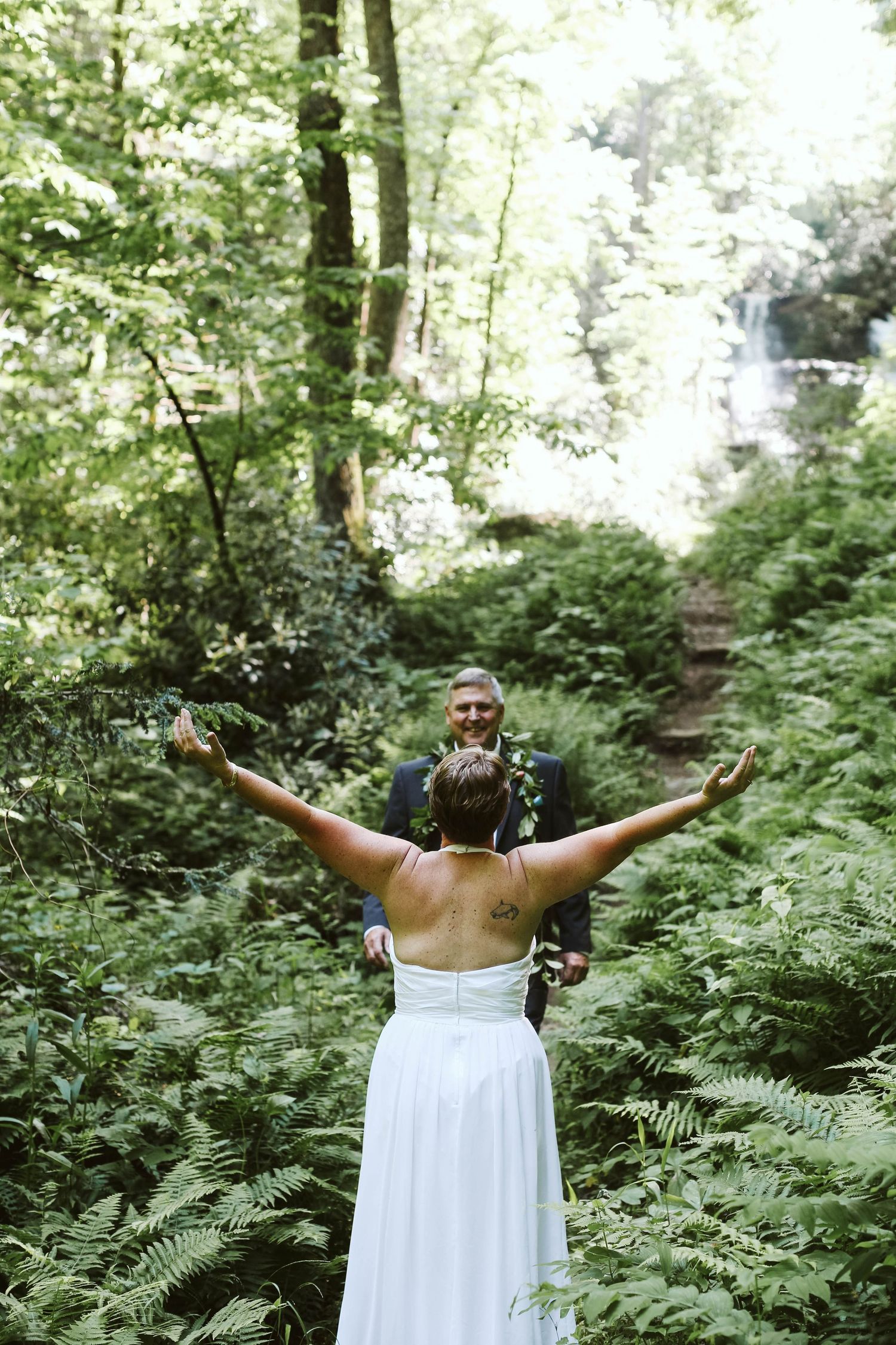 A person in a white dress stands with arms outstretched in a lush green forest.