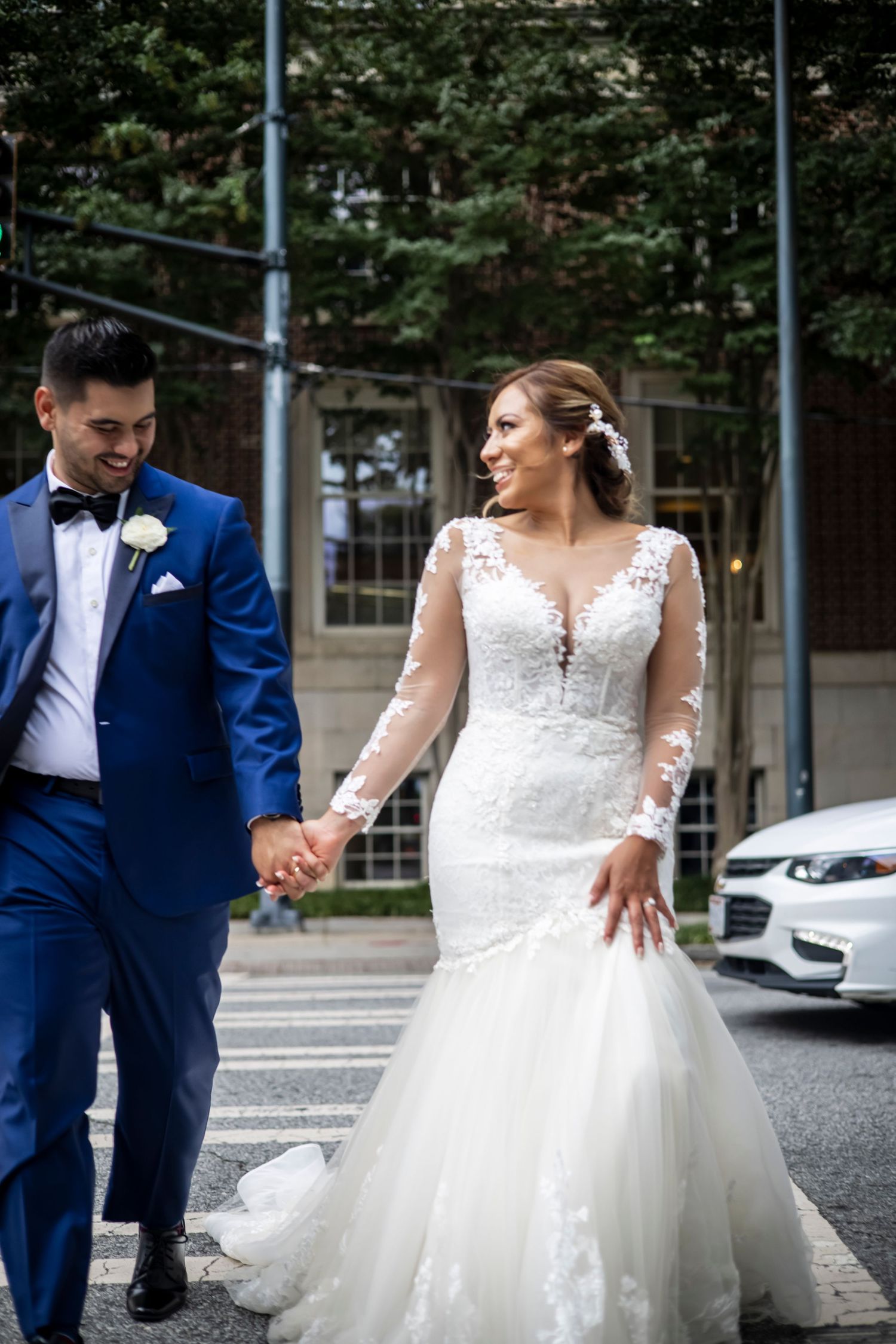 Wedding couple walking together outdoors, bride in lace dress and groom in blue suit.