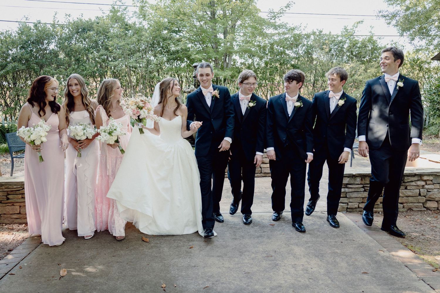 Wedding party in formal attire posing together outdoors with bridesmaids in pink dresses.