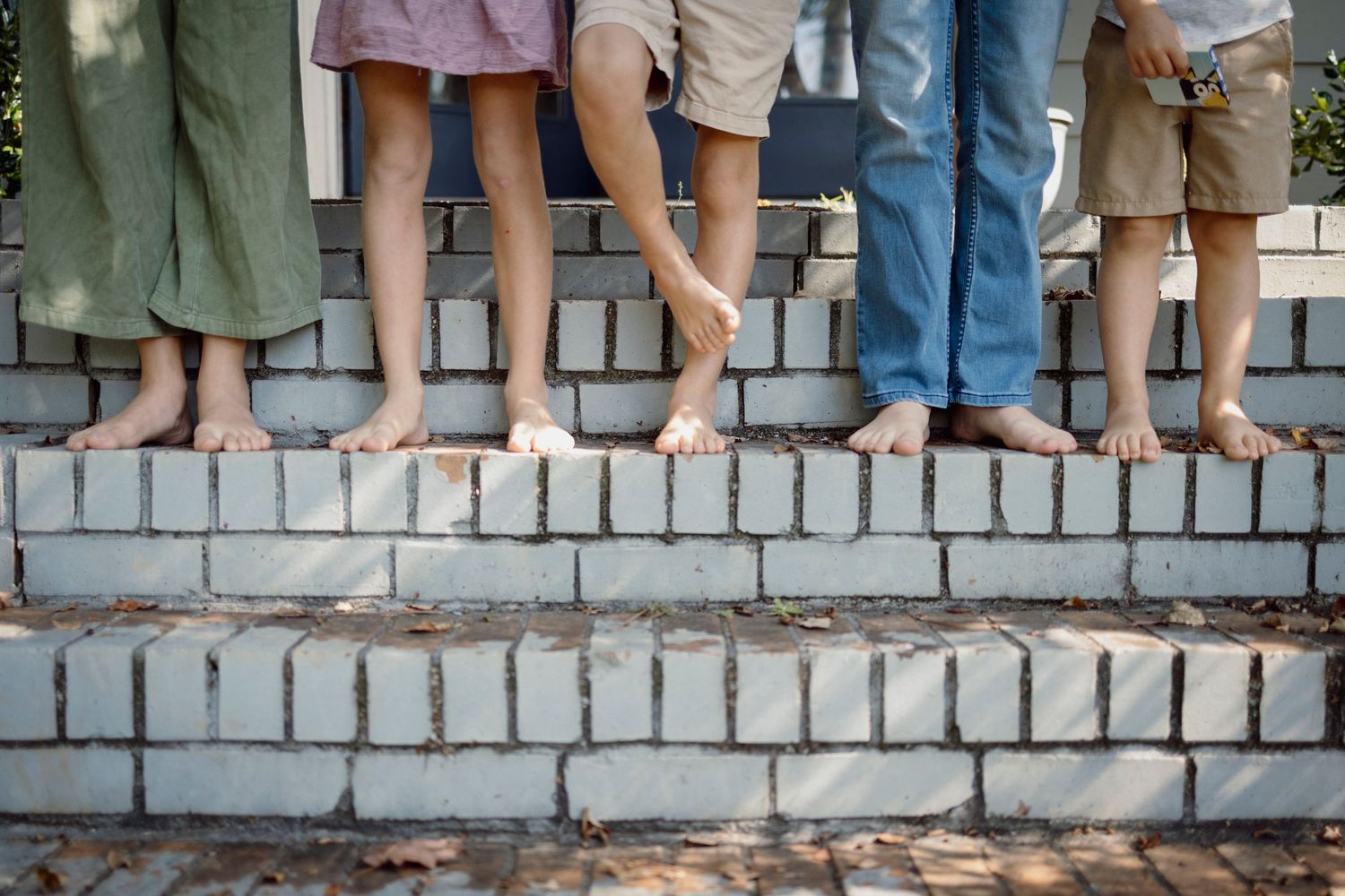 A row of legs and feet dangling over a stone wall shows people sitting together outdoors.