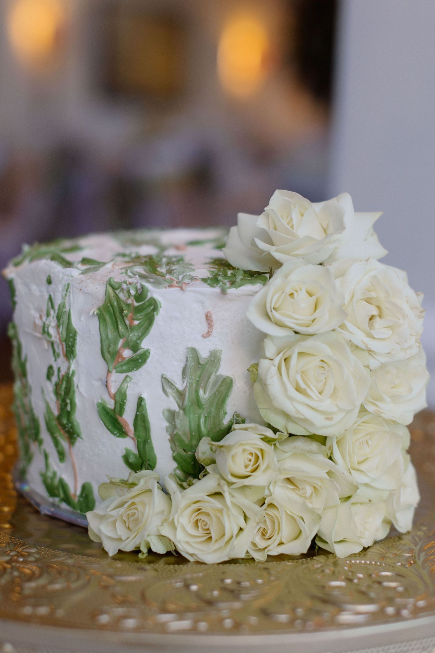 Elegant white wedding cake with green botanical painted design and fresh white roses cascading down the side.