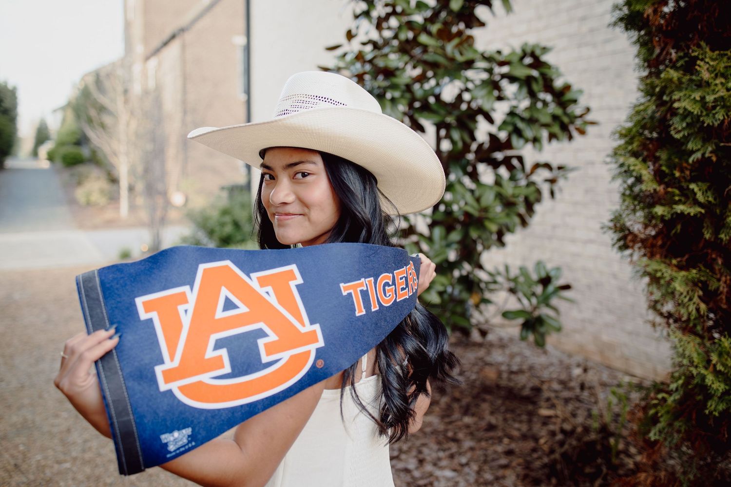 Young woman in a white cowboy hat holding an Auburn Tigers pennant flag outdoors.