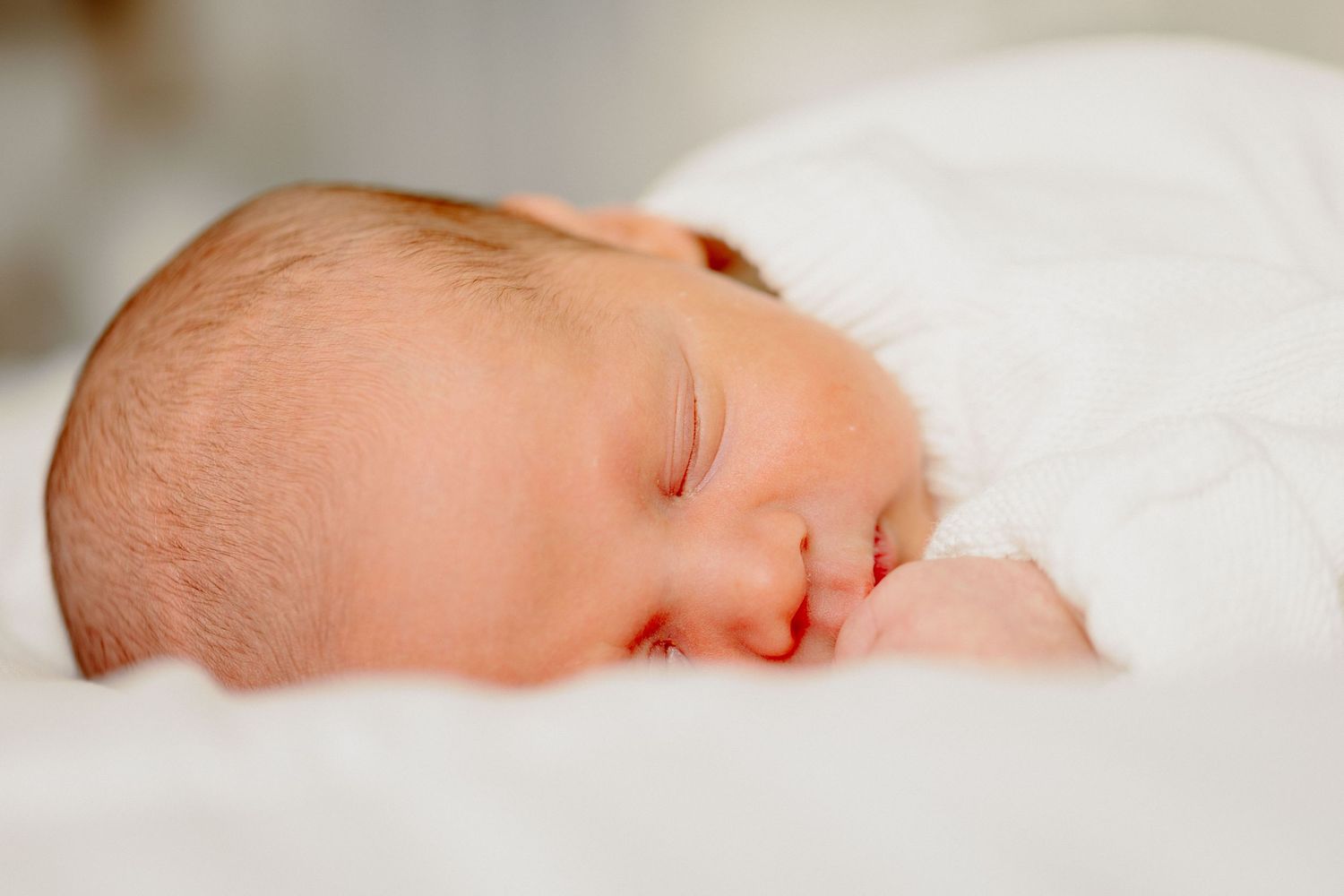 Sleeping newborn baby wrapped in soft white blanket with peaceful expression.