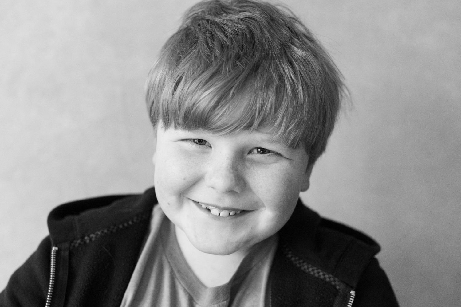 Black and white portrait of a young child smiling warmly while wearing a dark jacket.
