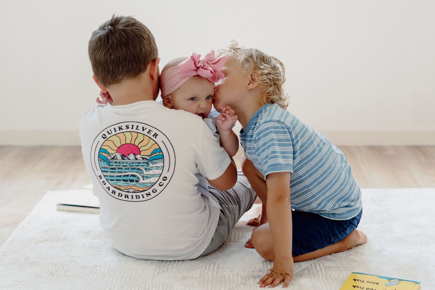 Two children in blue and white striped shirts play and read together on a light colored floor.