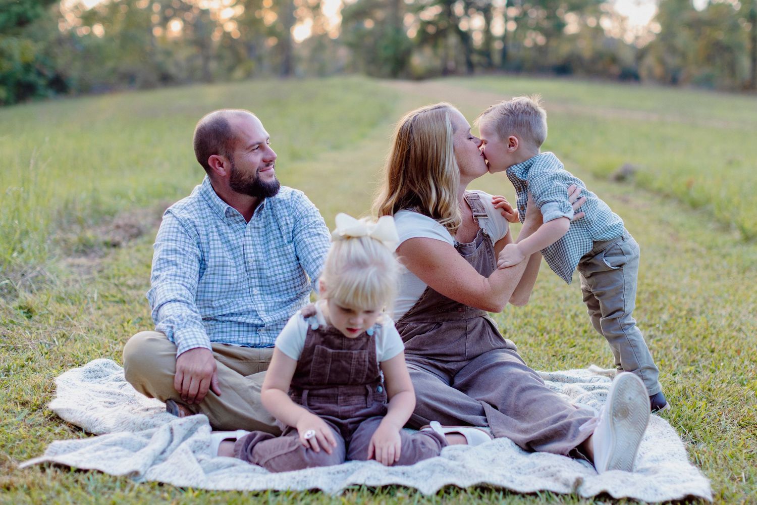 Family enjoying a relaxing picnic together on a blanket in a sunny meadow during golden hour.