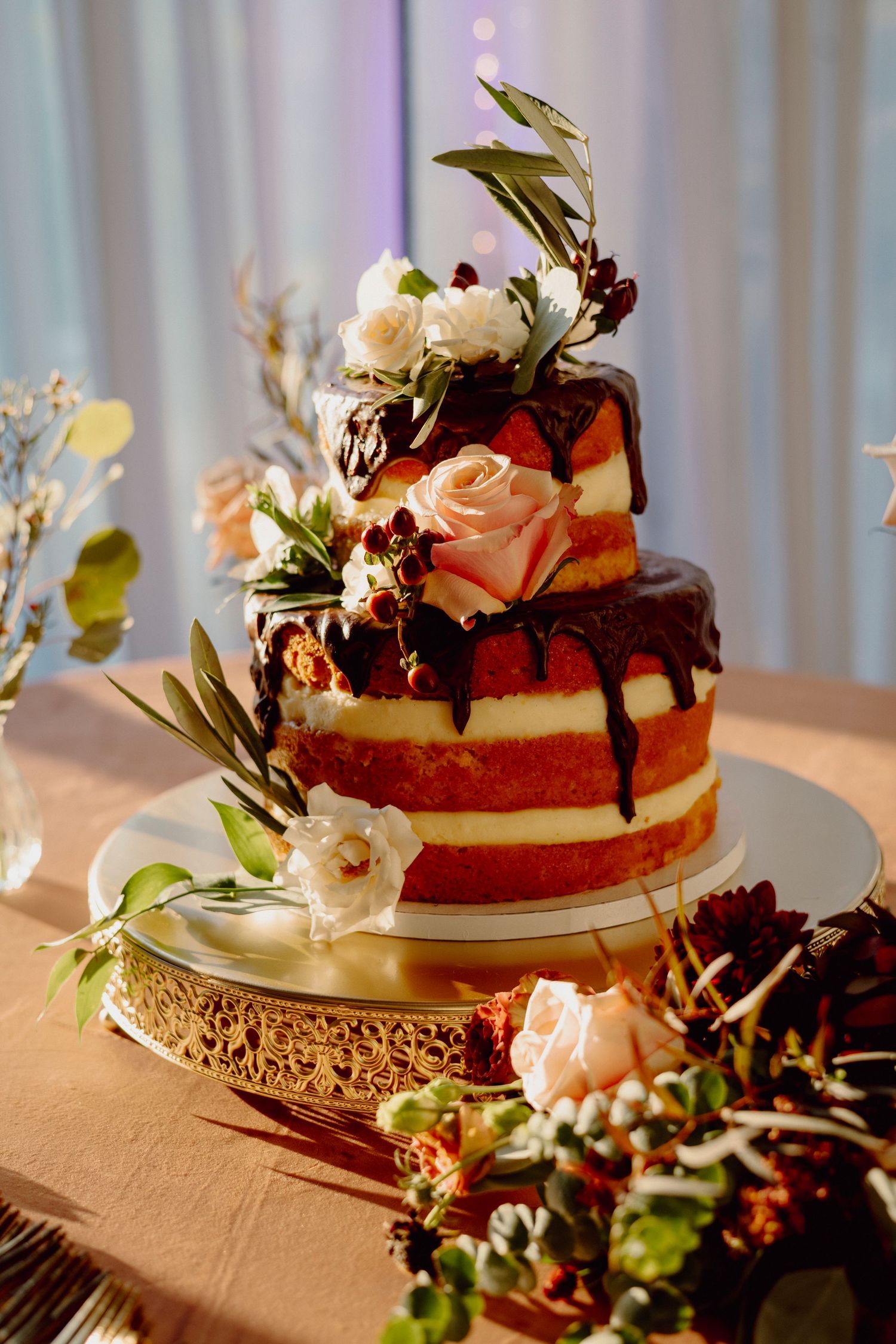 Elegant wedding cake decorated with fresh flowers and greenery on a rustic stand.