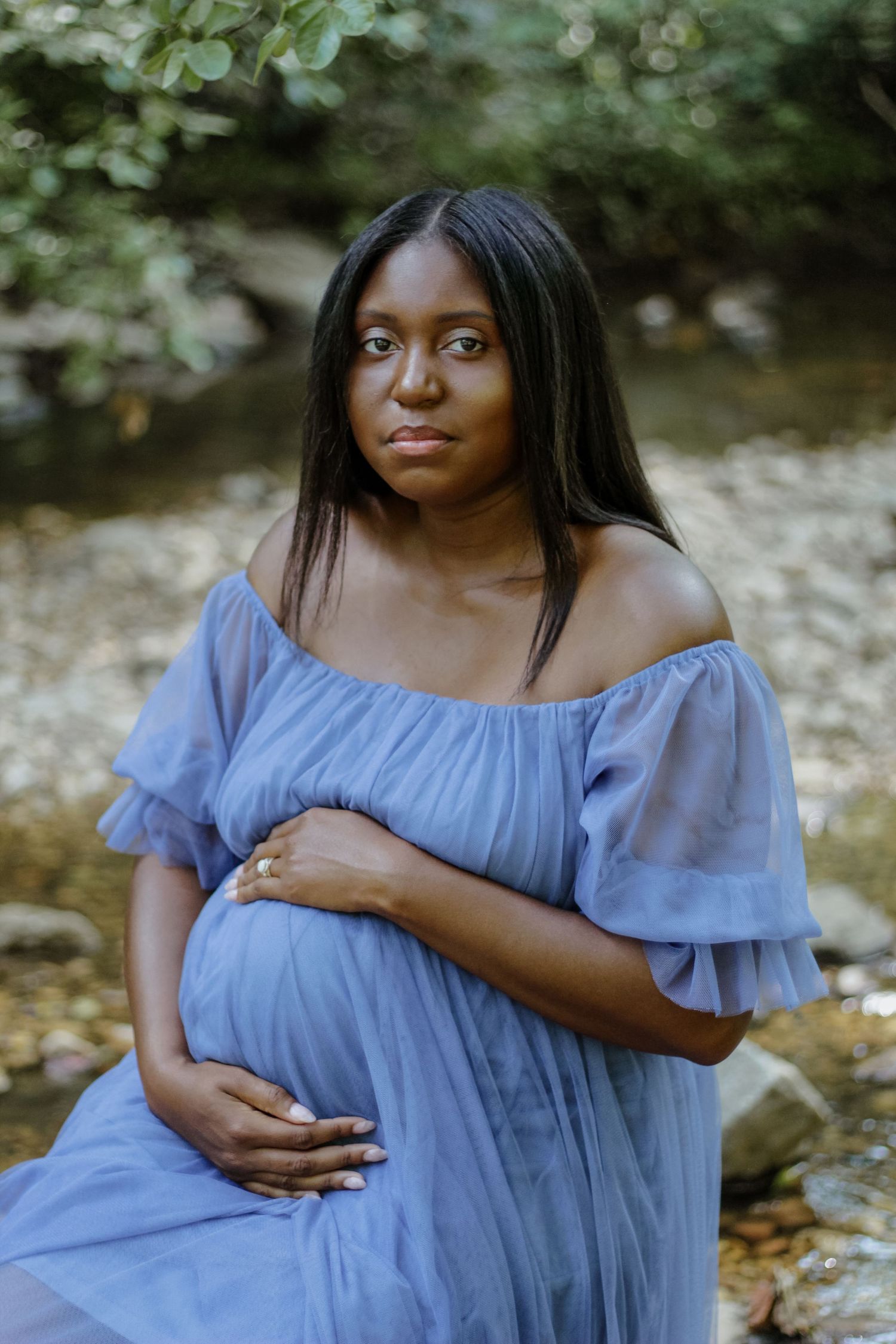 Woman in flowing blue dress poses elegantly during outdoor maternity photoshoot.