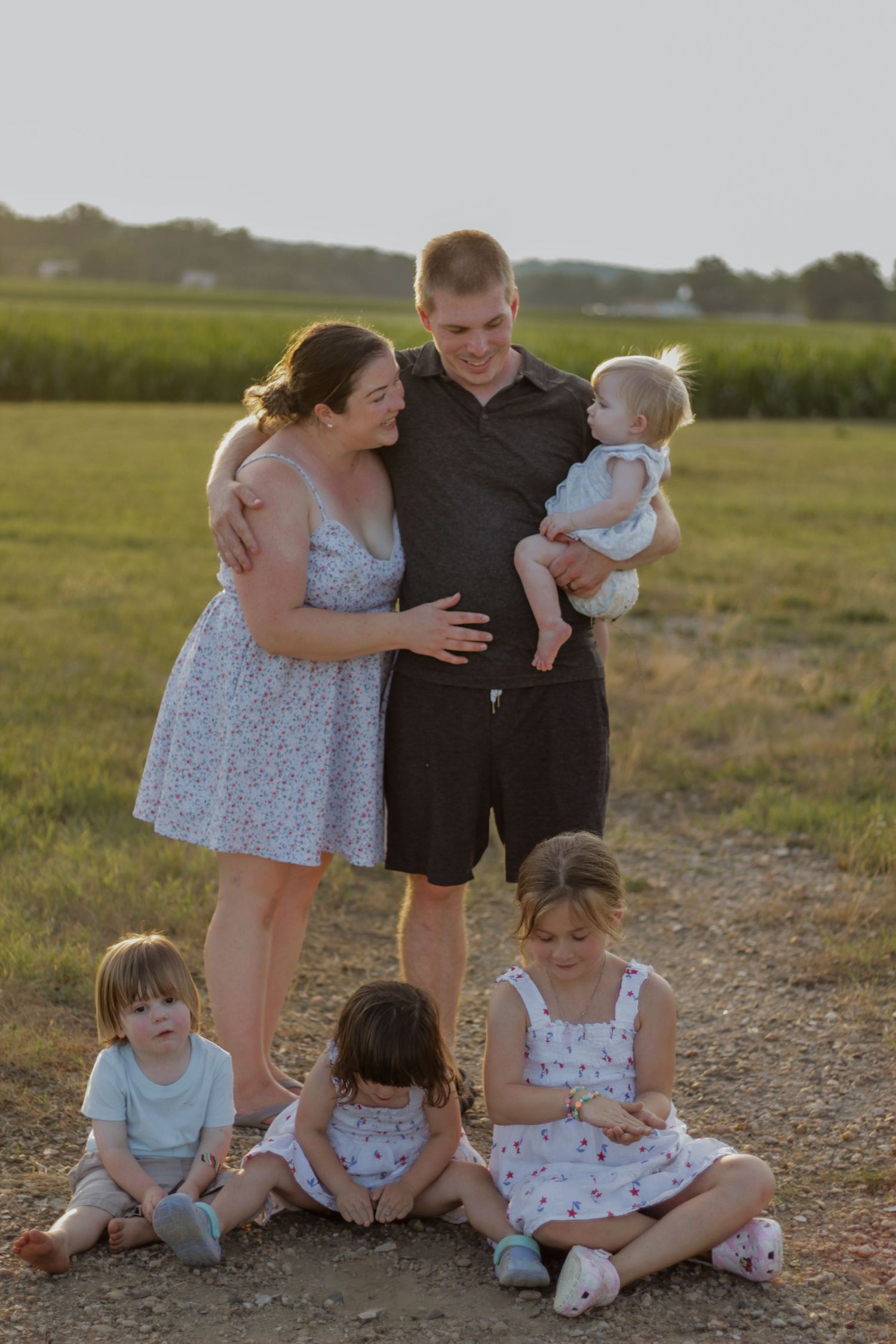 Family portrait of group sitting together outdoors at sunset in a field.