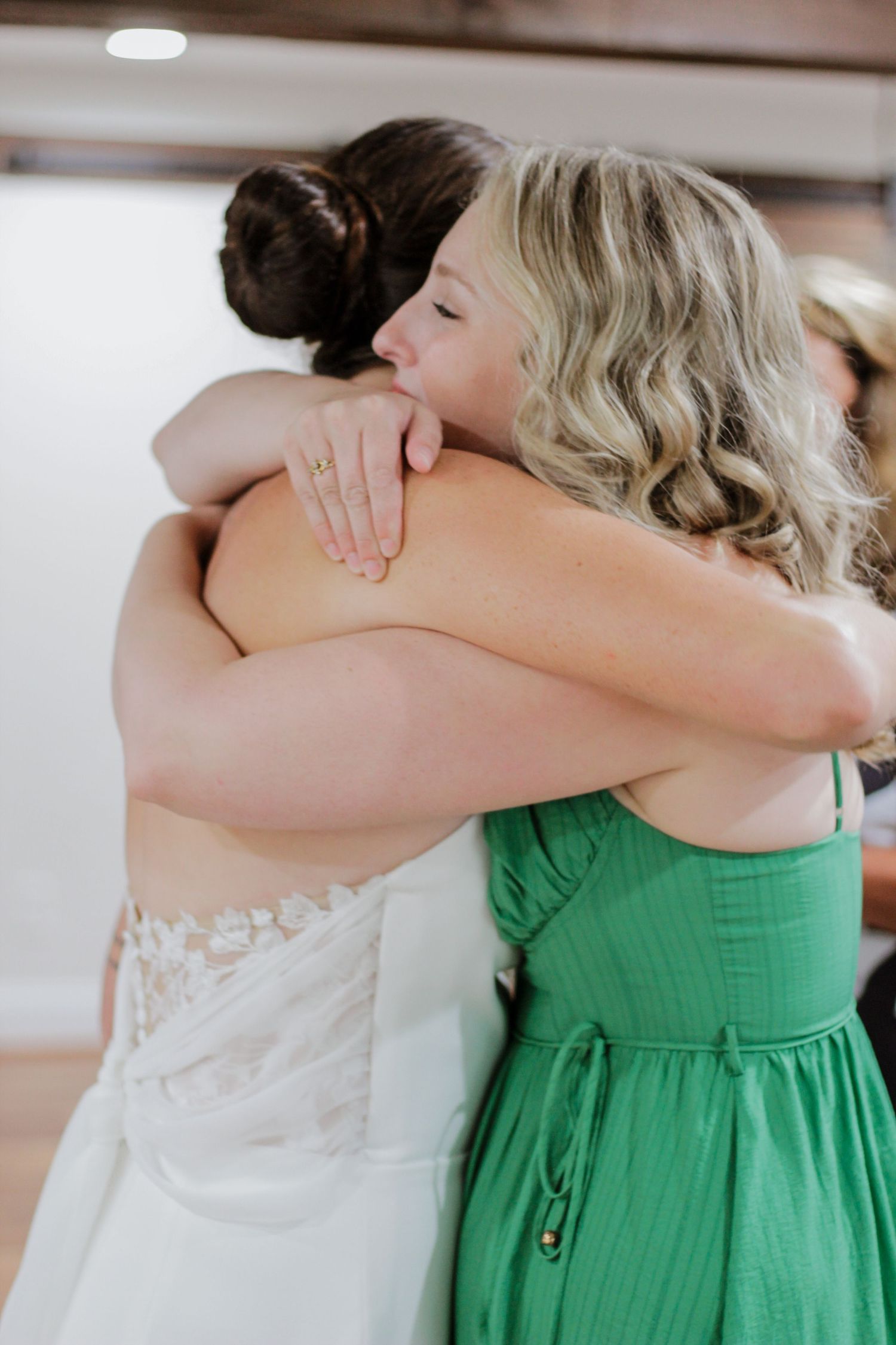 Wedding party members in white and emerald green dresses embrace in a touching moment.