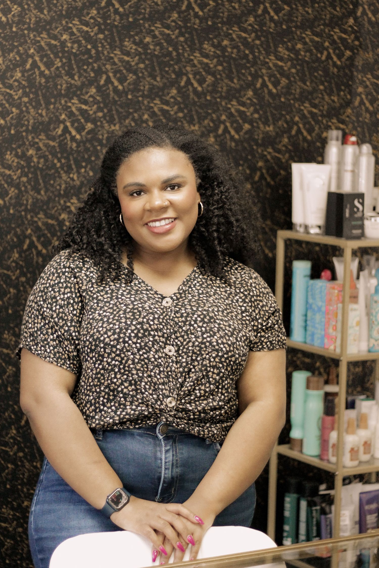 Person in leopard print blouse sits at desk with beauty products and shelving visible in background.