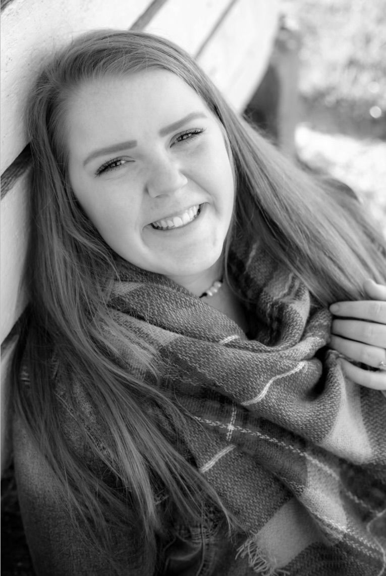 A black and white portrait of a person wearing a cozy knit scarf while smiling at the camera.