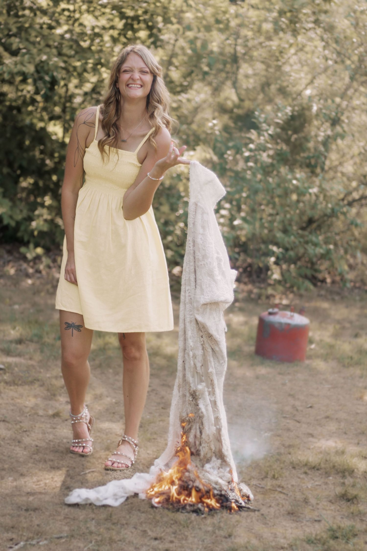 Someone in a pale yellow dress burns fabric over a small fire outdoors.