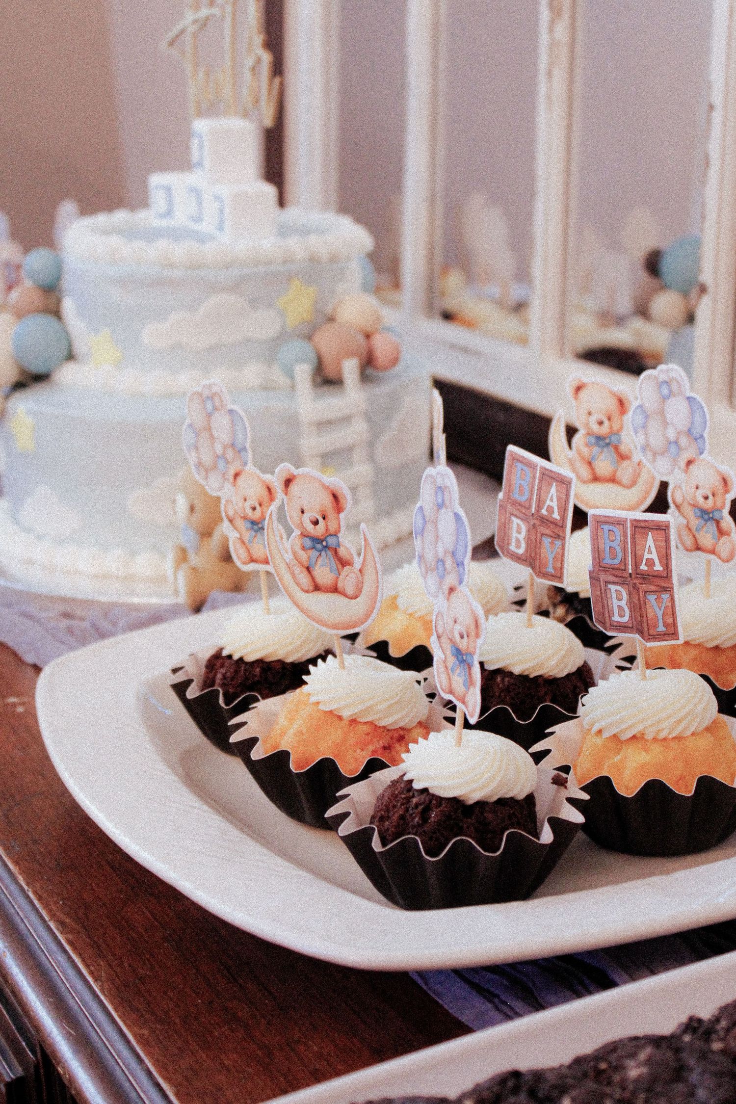 Cupcakes decorated with white frosting and teddy bear toppers at a baby shower dessert table.