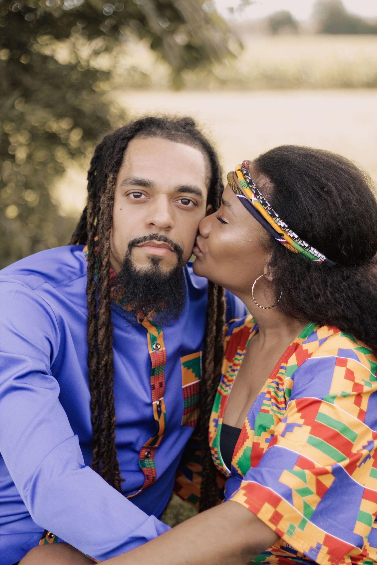 A couple in colorful African-inspired attire share an intimate moment outdoors.
