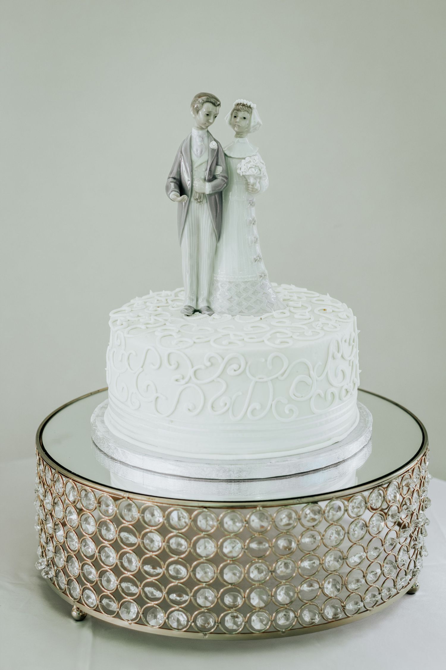 Classic white wedding cake with pearl-accented stand and traditional bride and groom topper.
