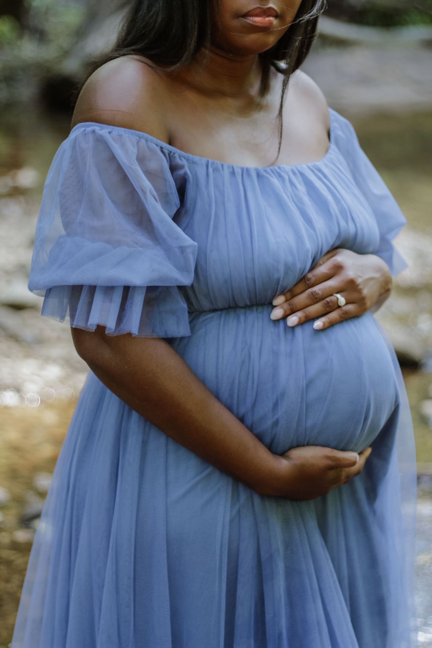 Woman in light blue maternity dress poses gracefully showing her baby bump.