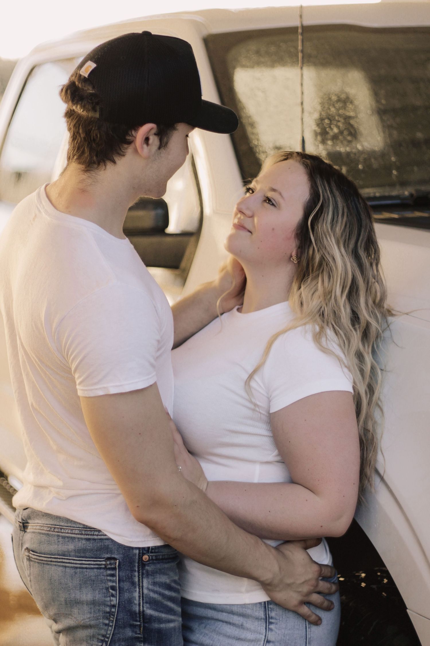 Couple in casual white shirts and jeans embrace against a car backdrop.