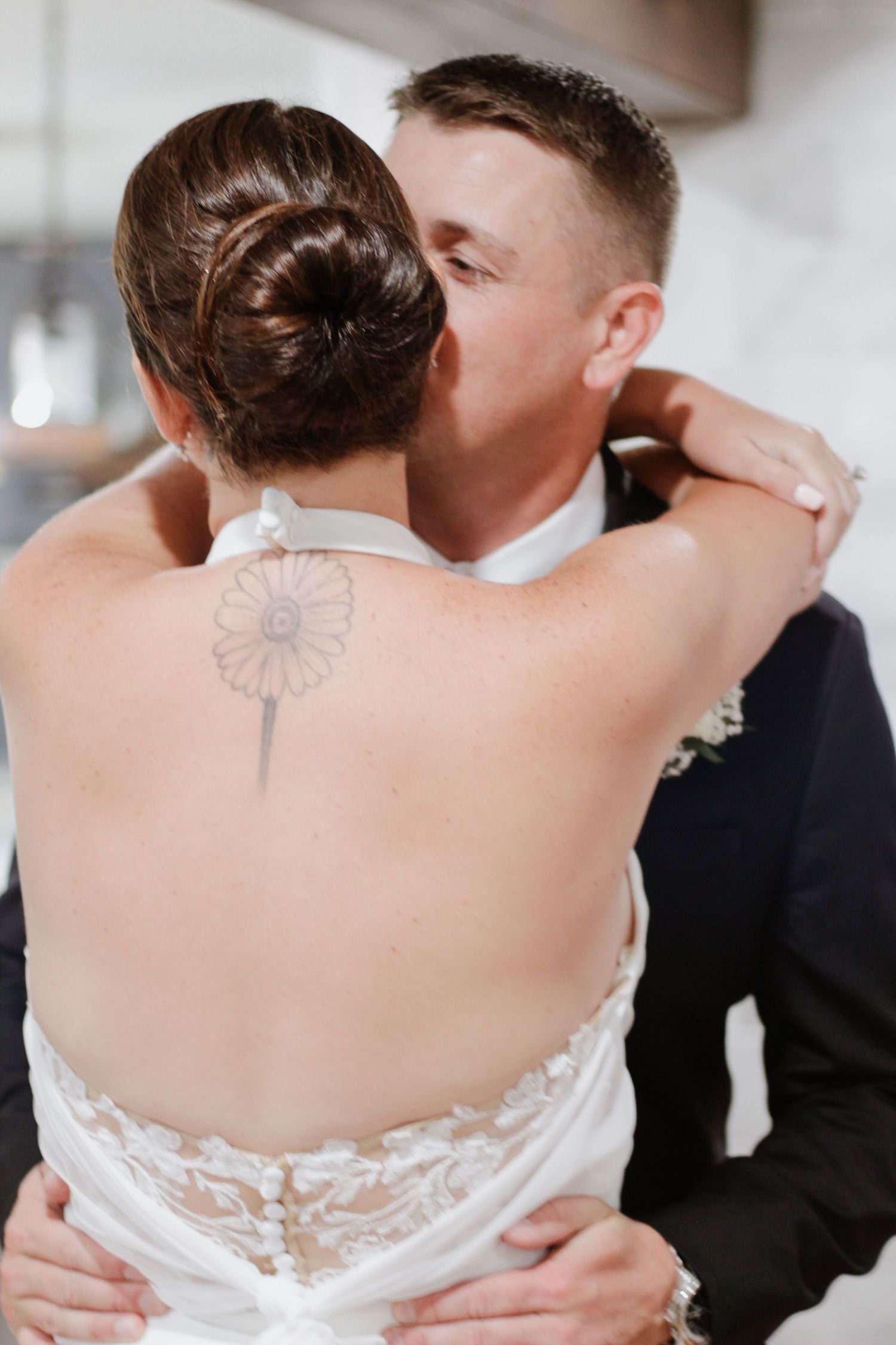 Close-up detail of a delicate white lace wedding dress back with a butterfly tattoo visible.