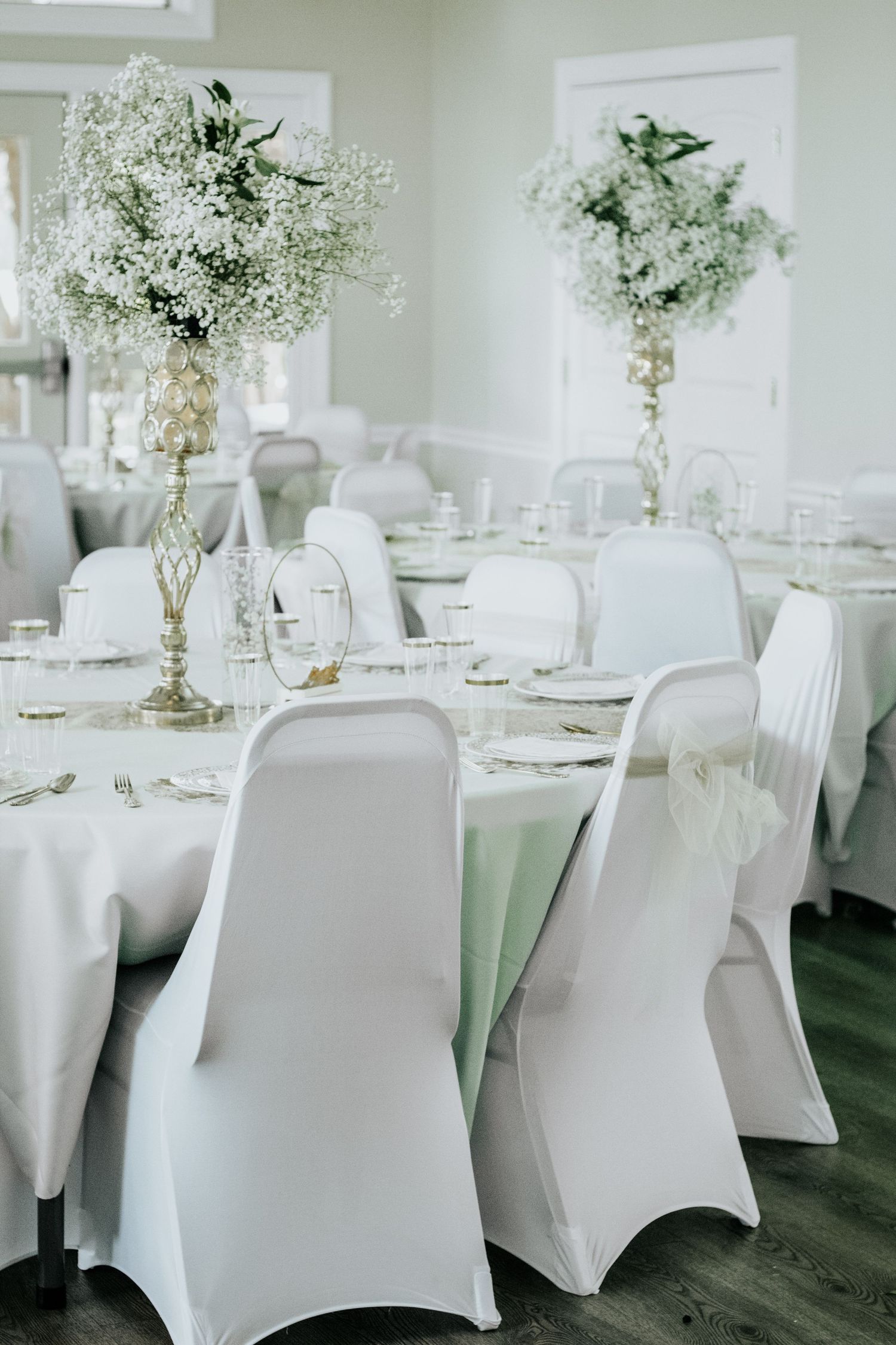 Elegant wedding reception tables with tall white floral centerpieces and spandex chair covers.