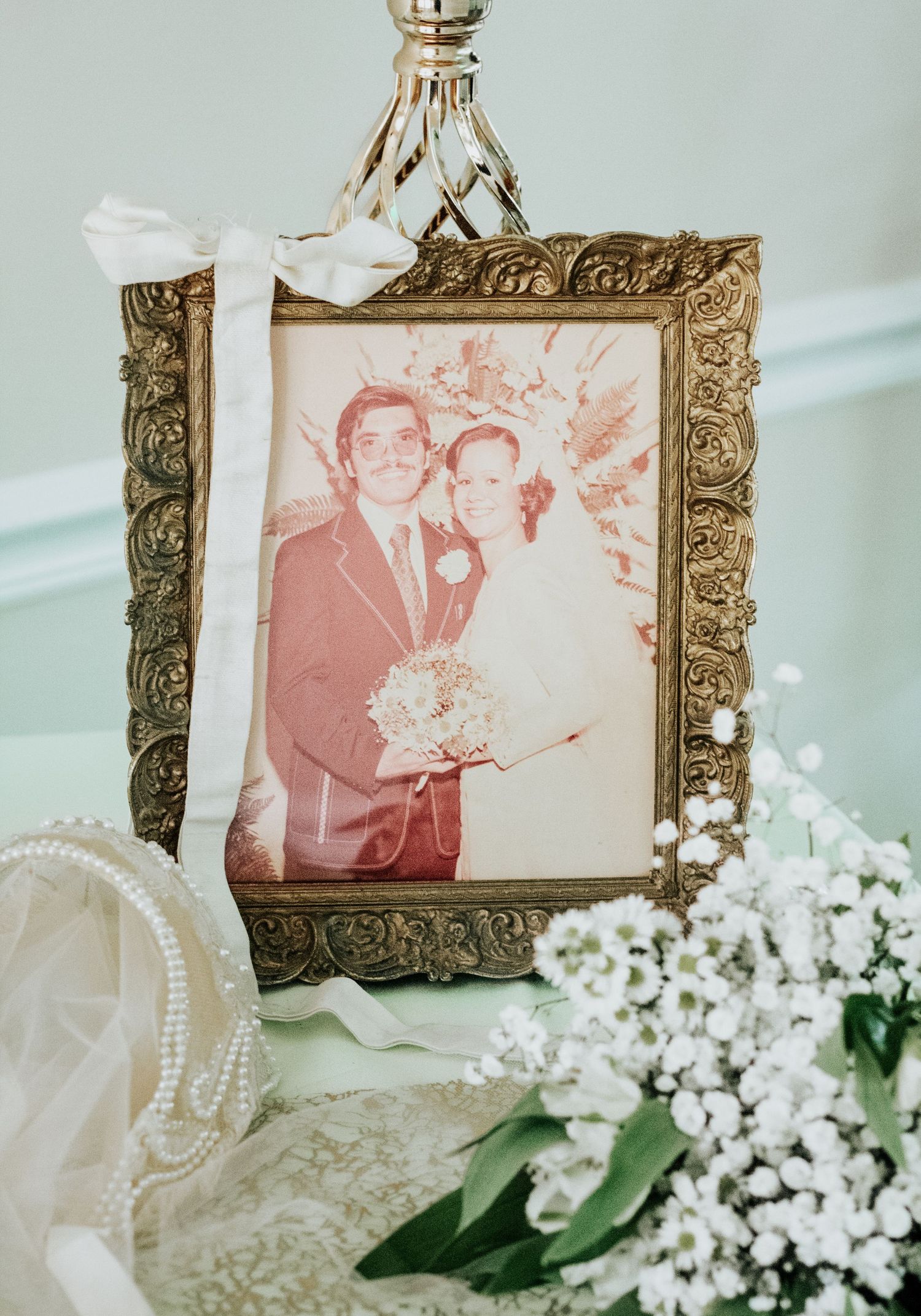 Vintage wedding photo in ornate gold frame surrounded by pearls and baby's breath flowers.