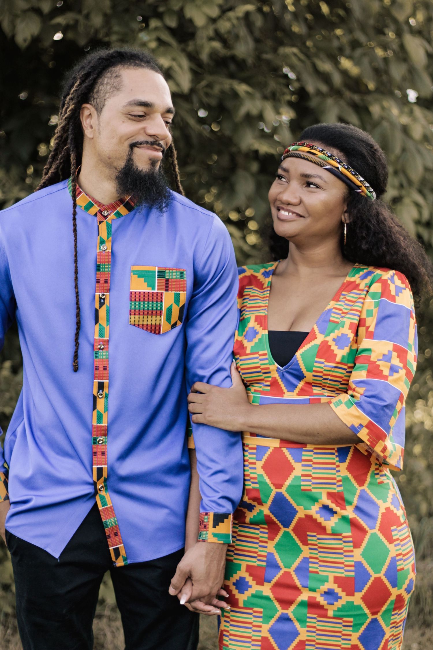 A couple in coordinated African print outfits smile while embracing outdoors.