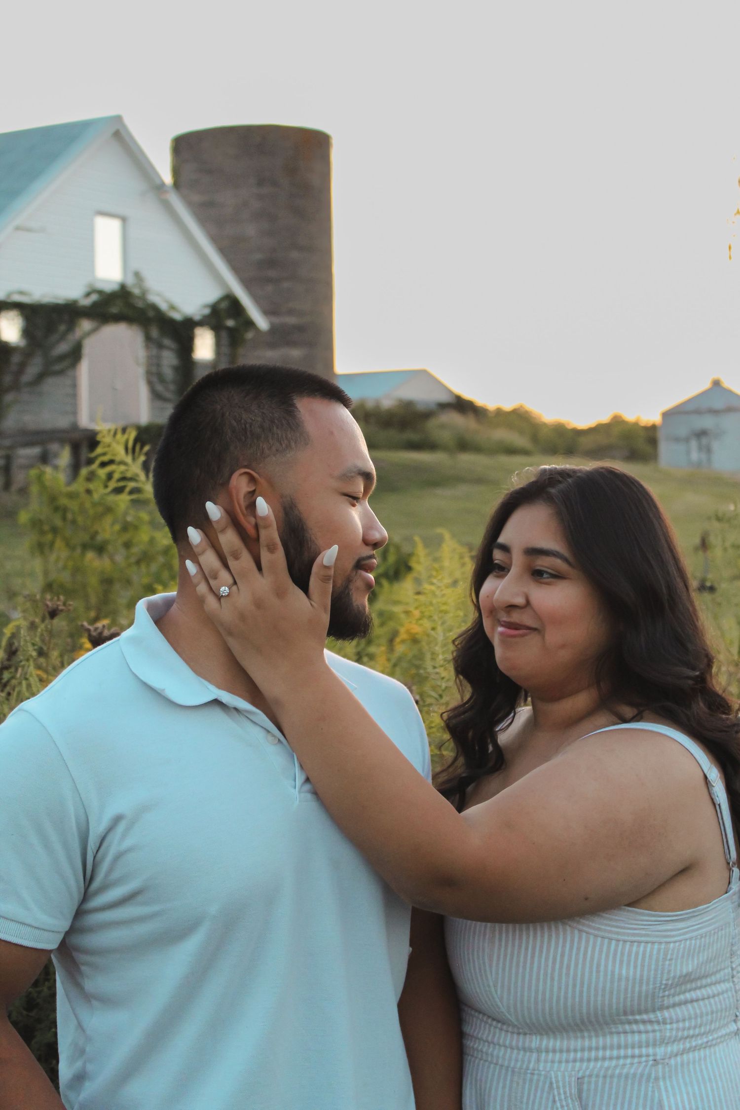 A romantic outdoor couple's portrait with a wooden silo and blue sky in the background.