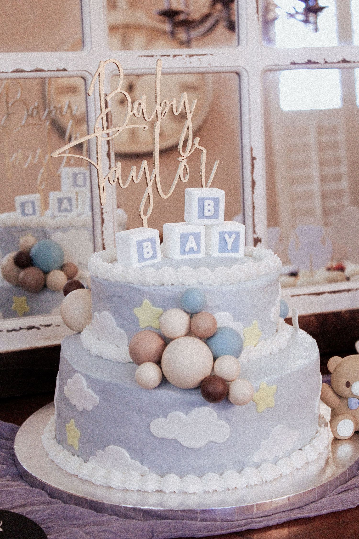 A two-tiered baby shower cake decorated with clouds, stars, and blue balloon decorations.
