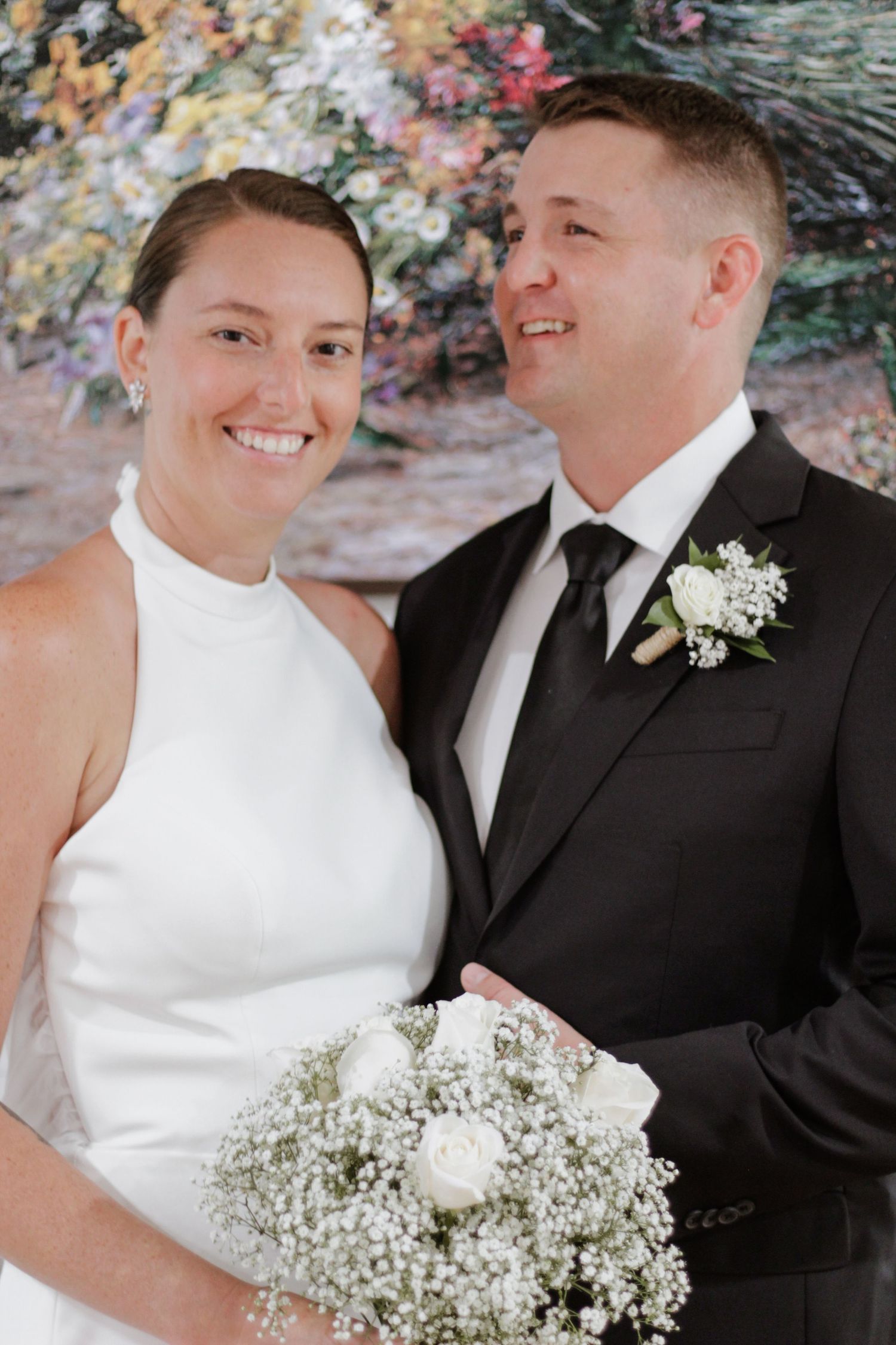 Wedding couple poses outdoors with bride holding white and baby's breath bouquet.