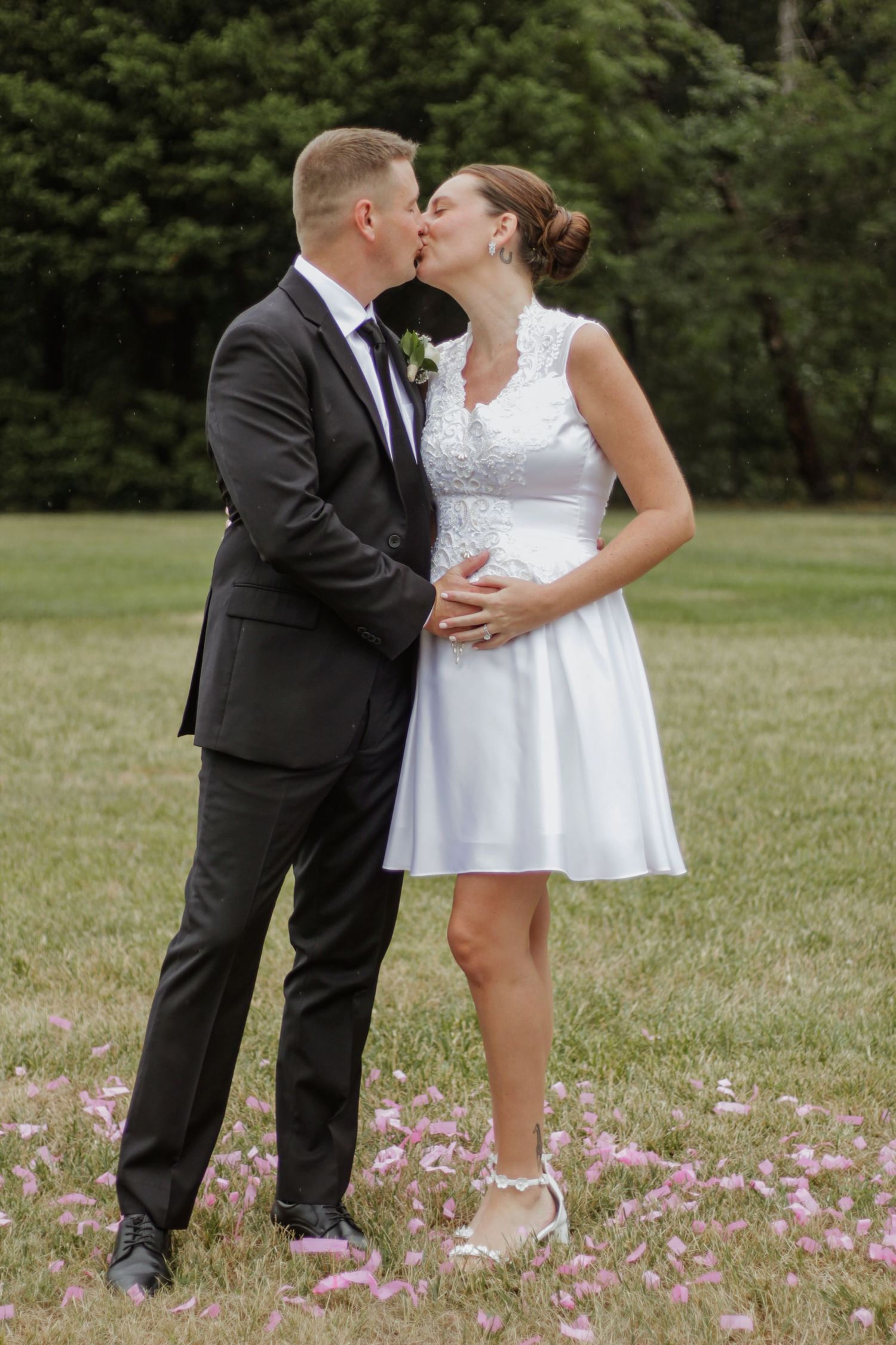 Couple in wedding attire sharing romantic moment among pink flower petals.