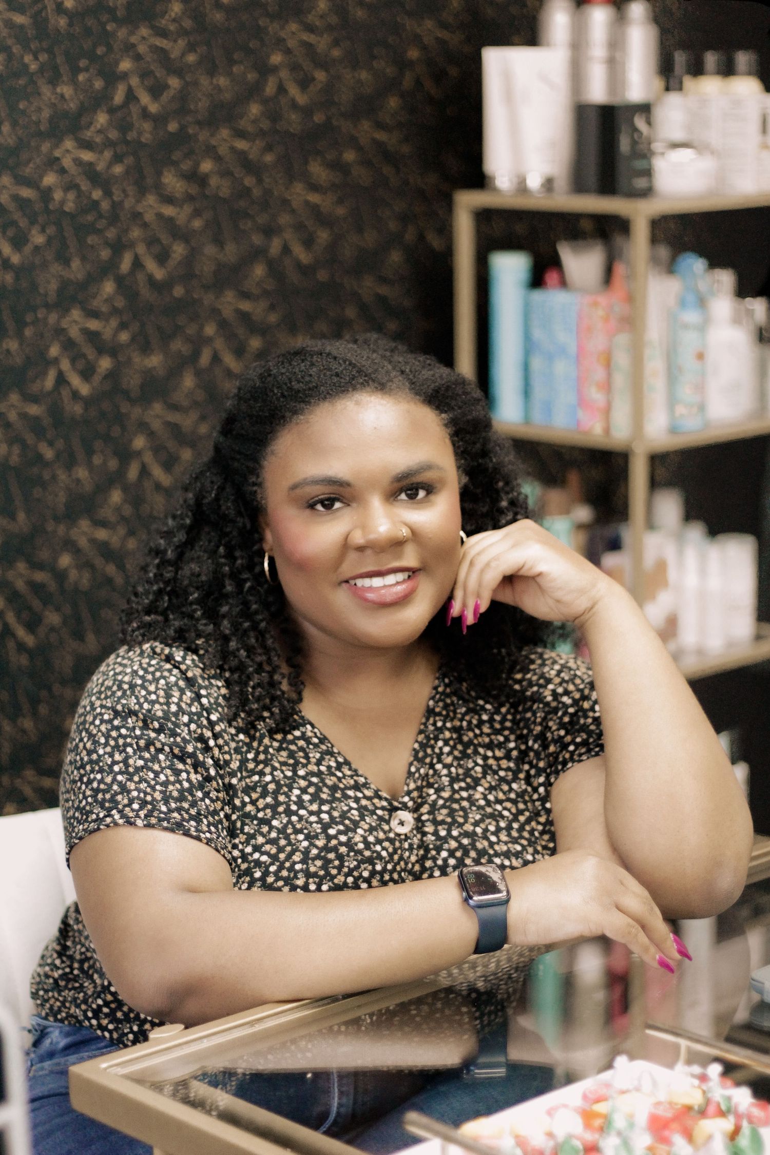 Person in leopard print top smiles warmly while sitting at desk with beauty products visible in background.