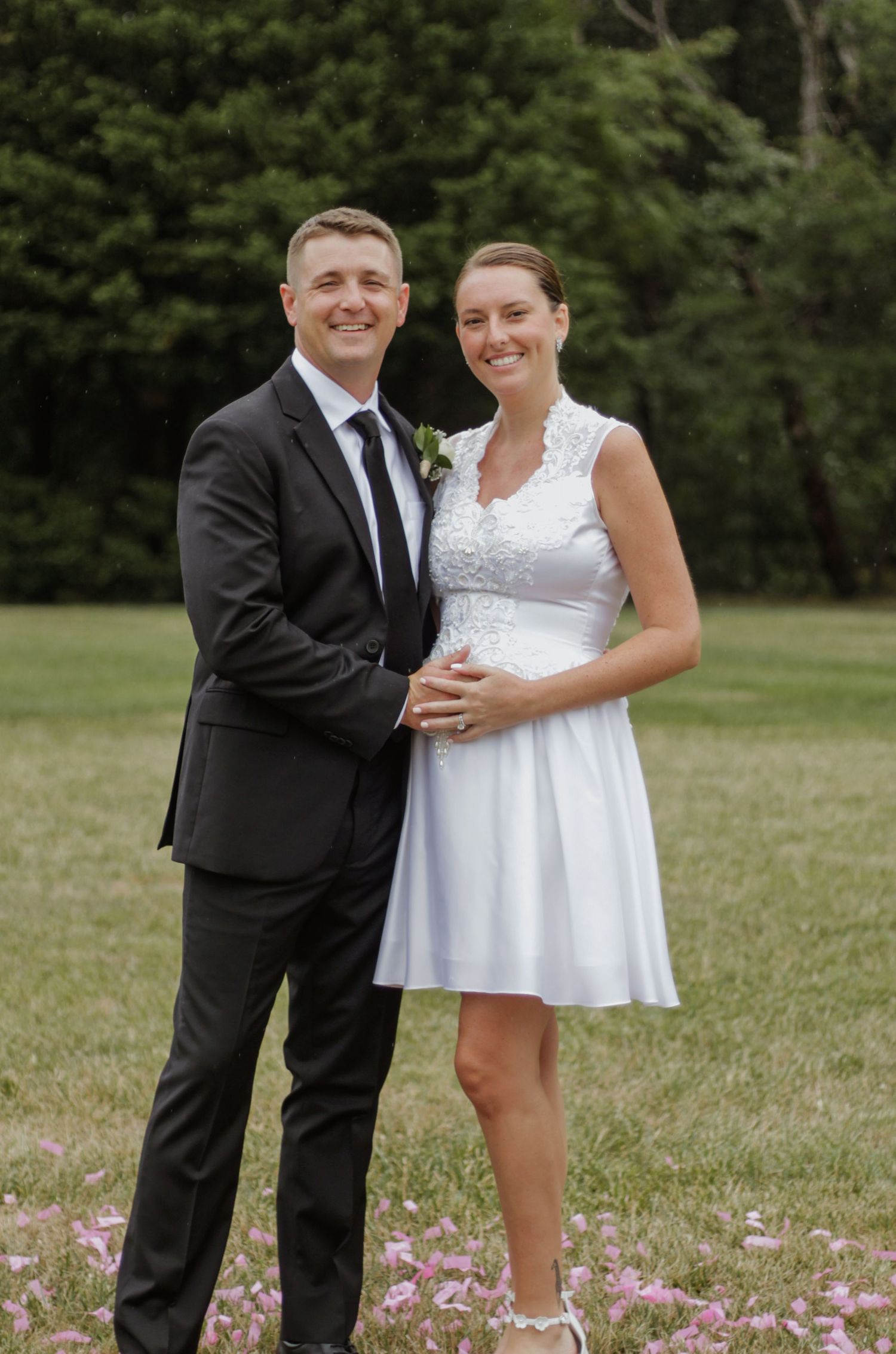 Couple in formal wedding attire posing together in a field with flowers.