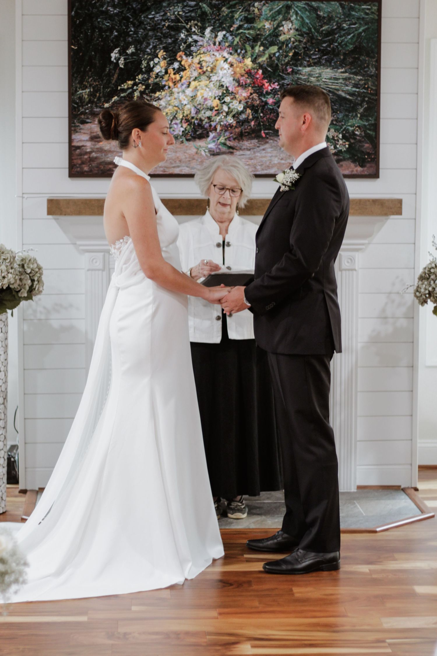 Indoor wedding ceremony taking place in bright white room with wooden floors.