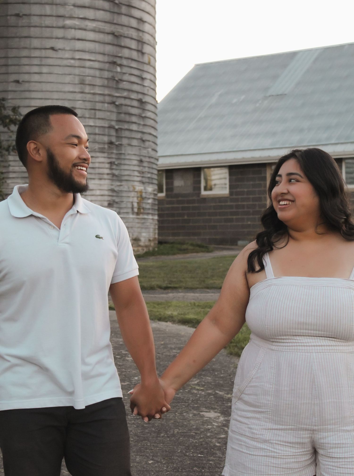 Casual engagement photos of couple in white outfits near rustic brick building.