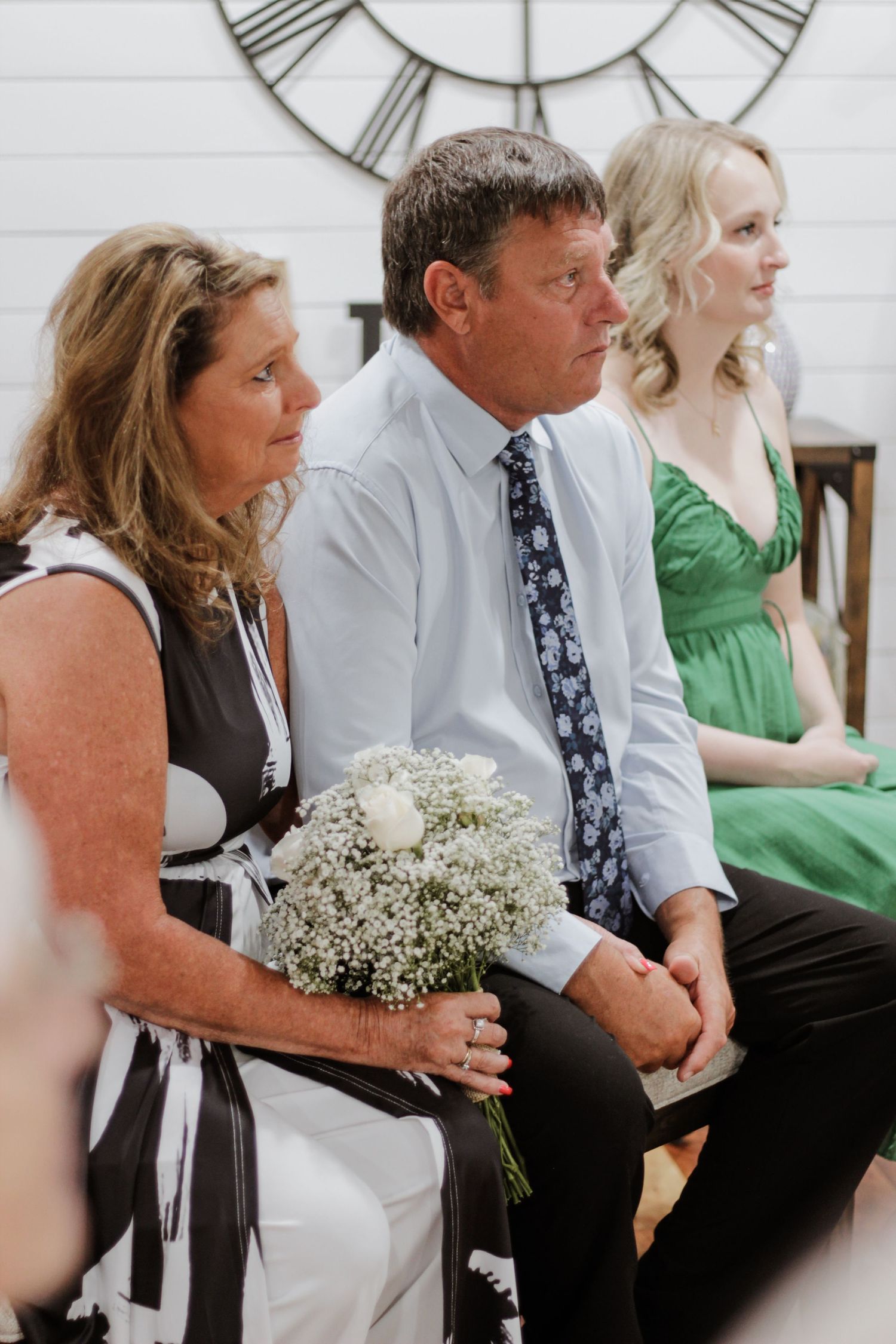 Wedding guests seated beneath large wall clock during ceremony.