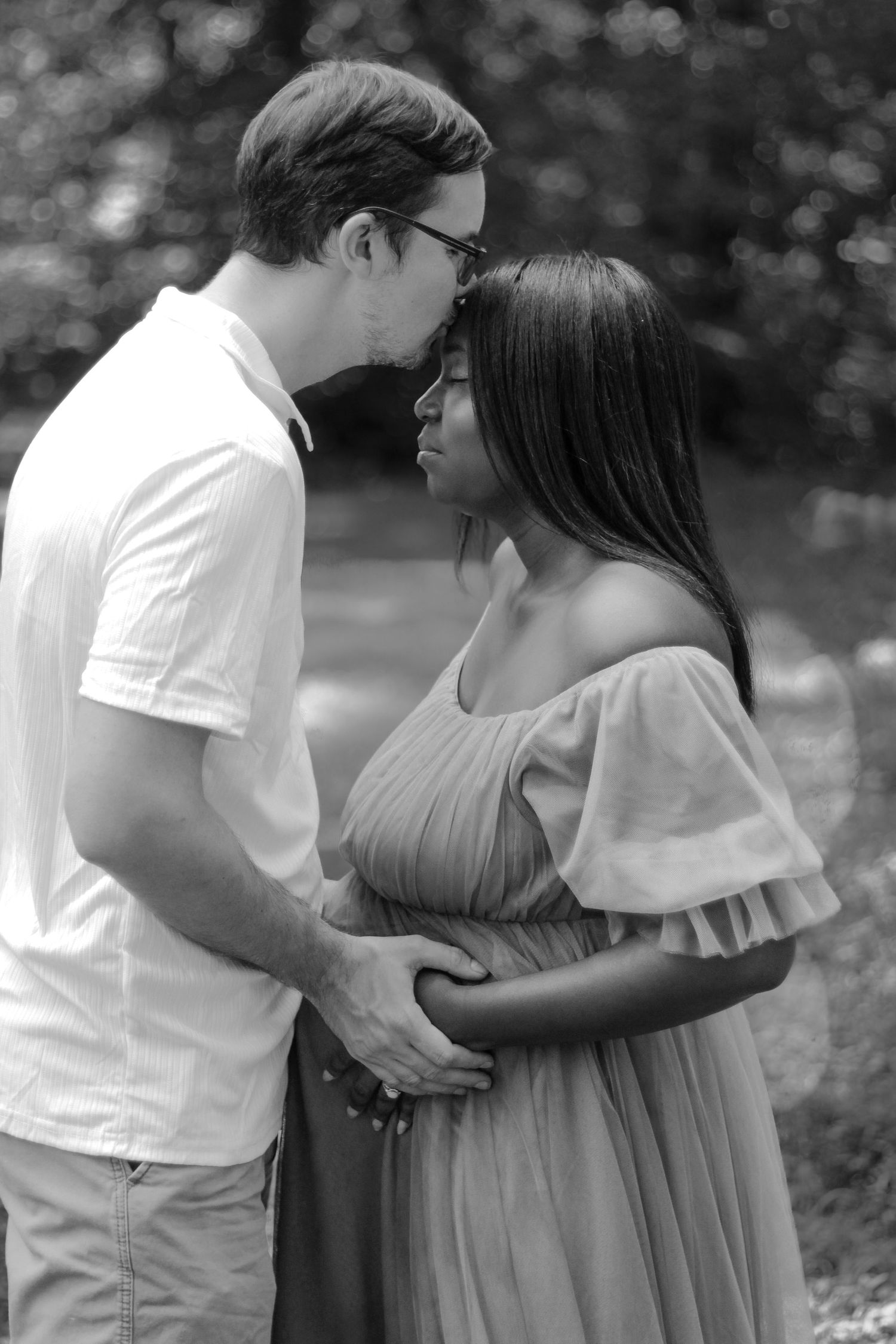 A romantic black and white portrait of a couple embracing outdoors showing a tender intimate moment between them.