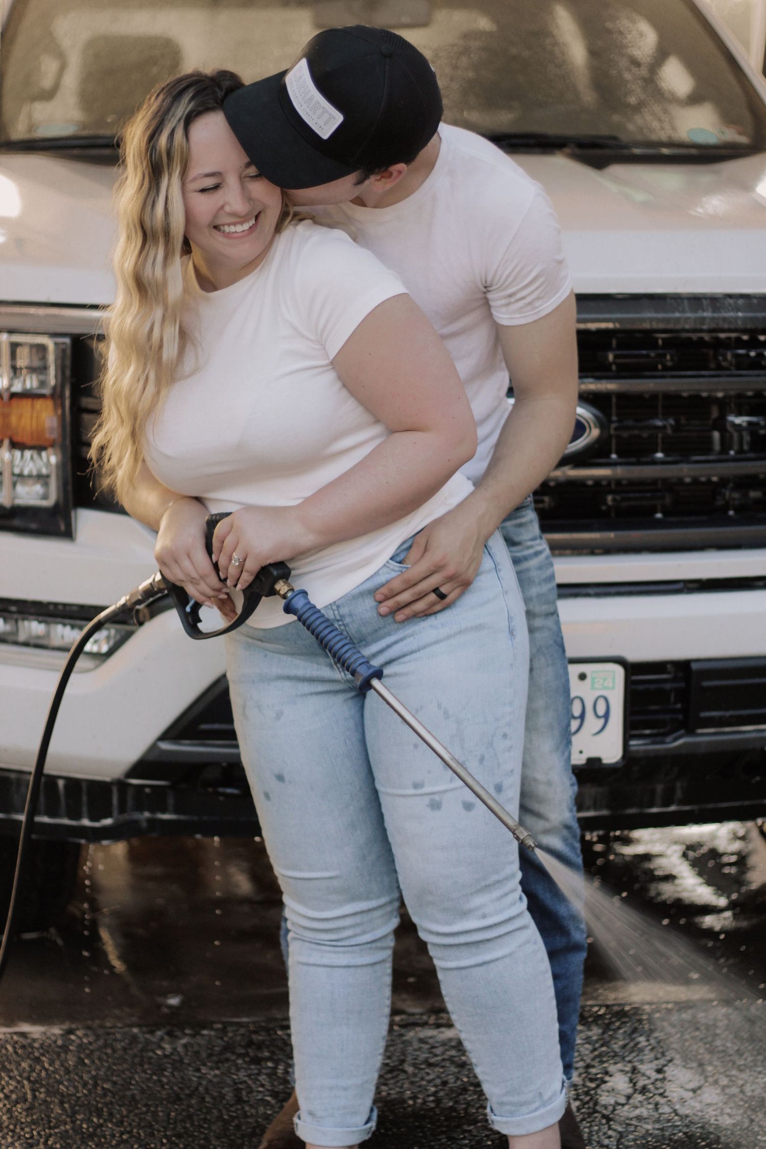 Couple washing car together with hose and soap in driveway.