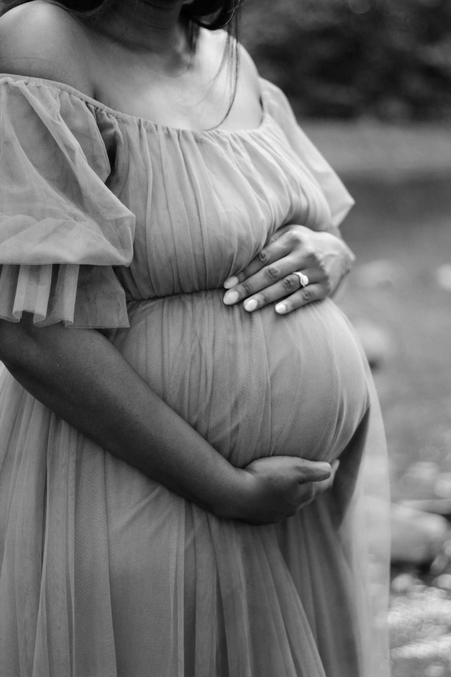 Black and white maternity photos showing hands cradling a pregnant belly in a flowing dress.