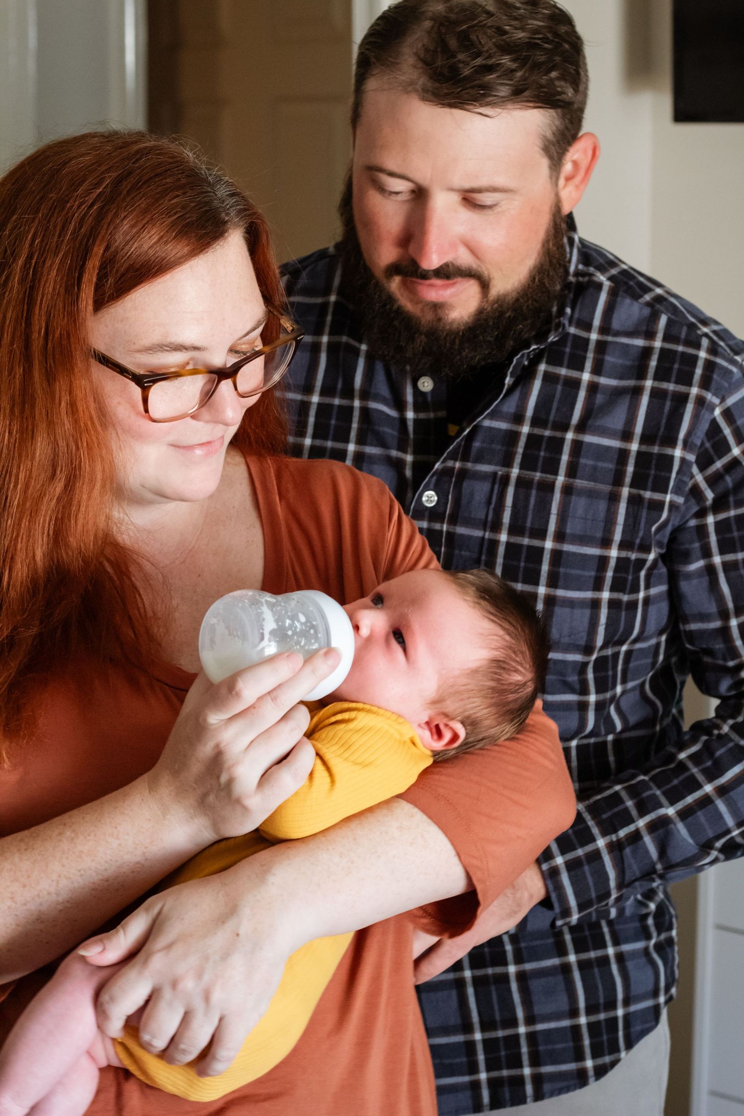 Parents tenderly feeding their newborn baby who wears a bright yellow outfit.