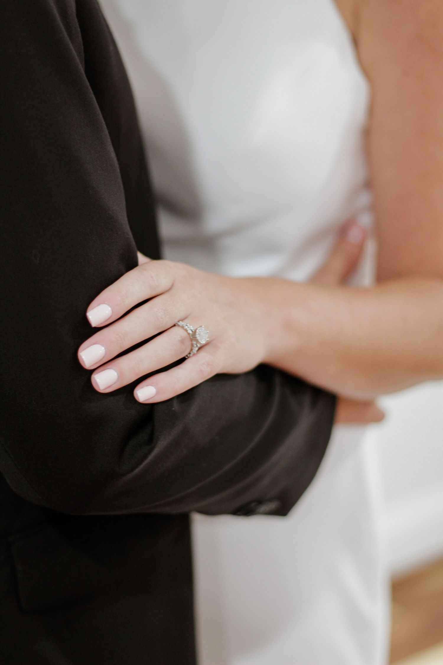 Close-up of hands and engagement ring against formal black and white wedding attire.