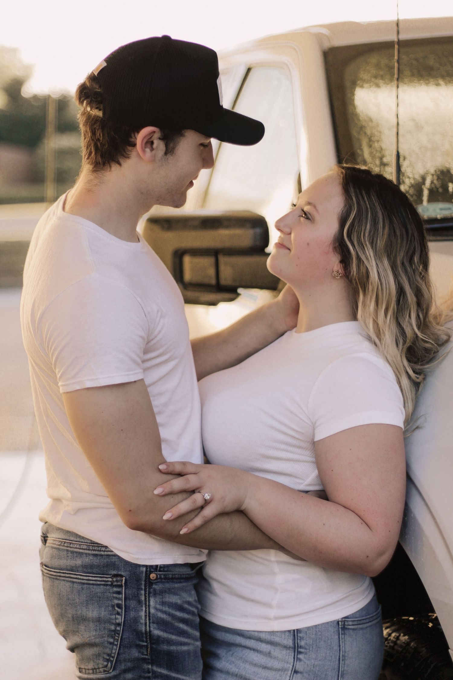 Romantic couple in white t-shirts embracing by vintage truck at sunset.